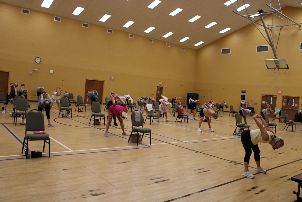 A gymnasium full of people working out and stretching with the use of chairs
